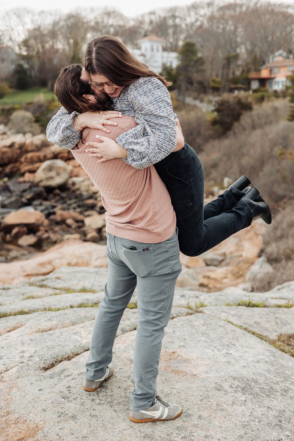 Couple sharing a joyful embrace on rocky terrain, man lifting woman as they hug outdoors.