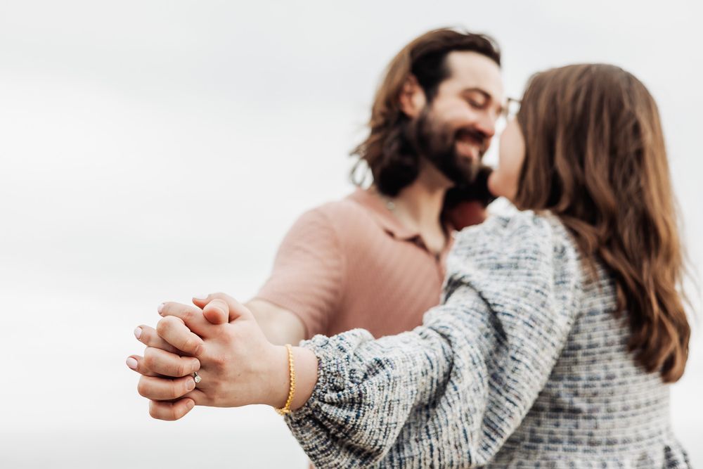 Couple dancing outdoors holding hands, man in pink shirt and woman in gray tweed jacket sharing a romantic moment.