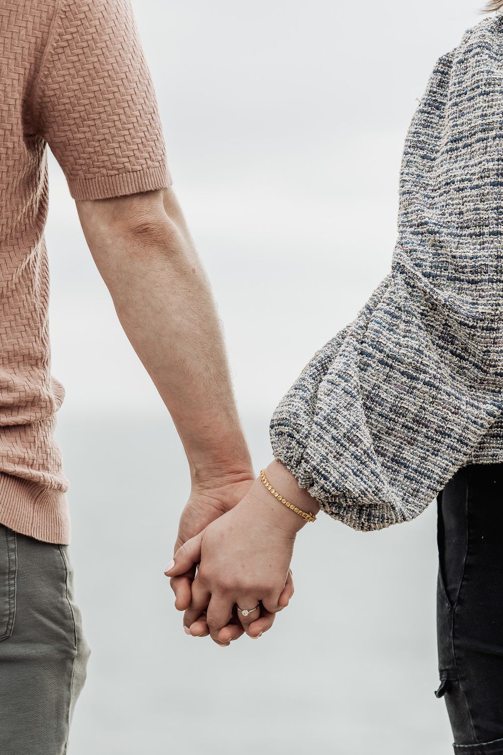 Close-up of a couple holding hands, woman wearing a gold ring and bracelet.