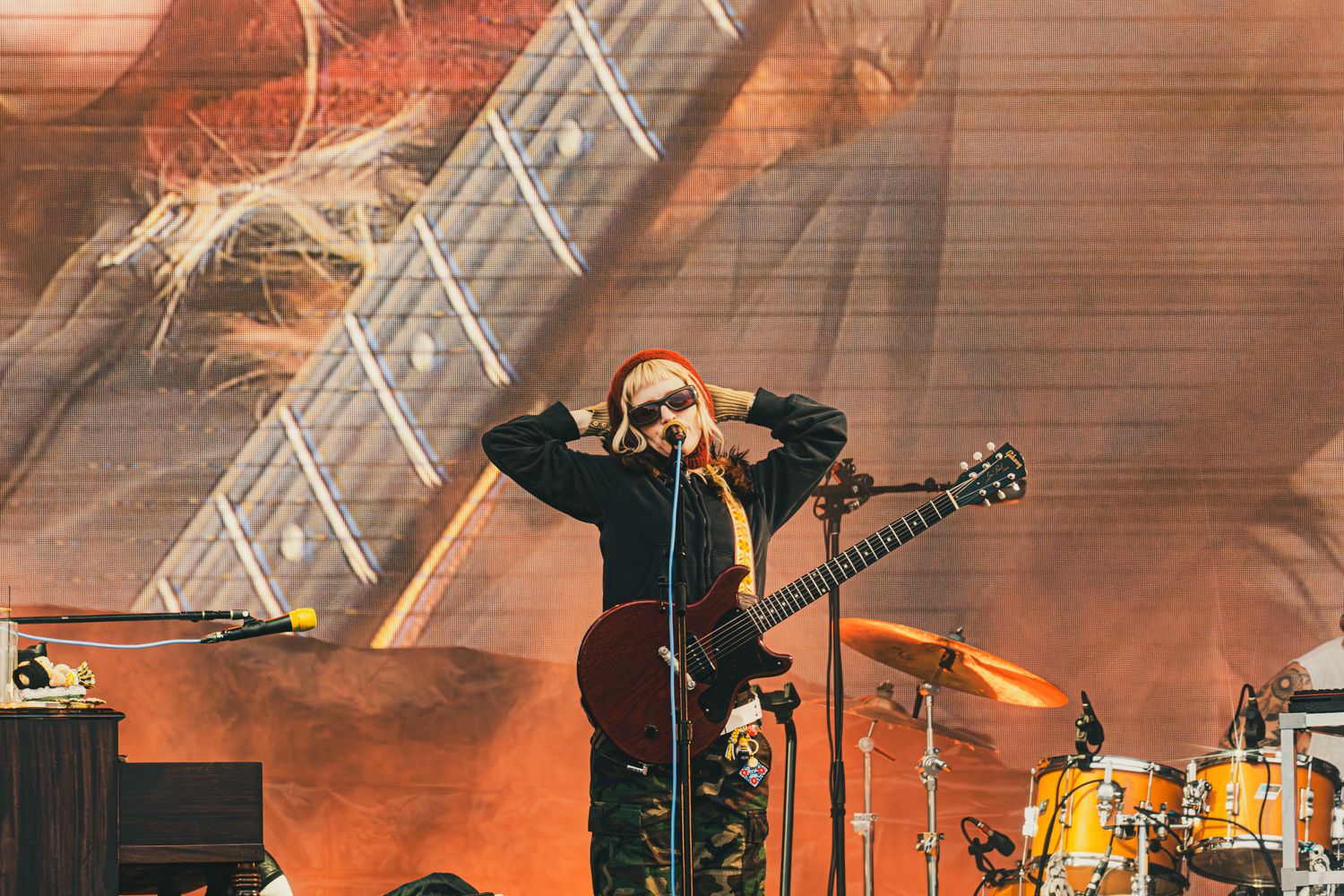 Guitarist performing on stage with a large guitar backdrop at an outdoor music festival.