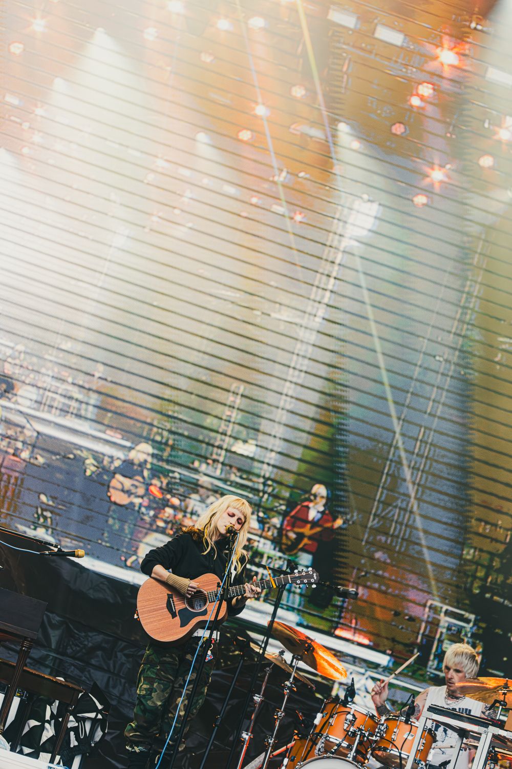 Blonde female guitarist performs on stage with dramatic lighting at a live concert event.