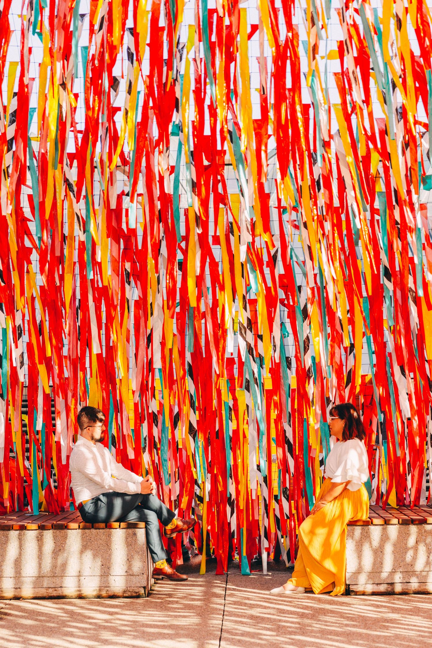 Two people sitting beneath a vibrant installation of red, orange and yellow streamers creating a dramatic backdrop.