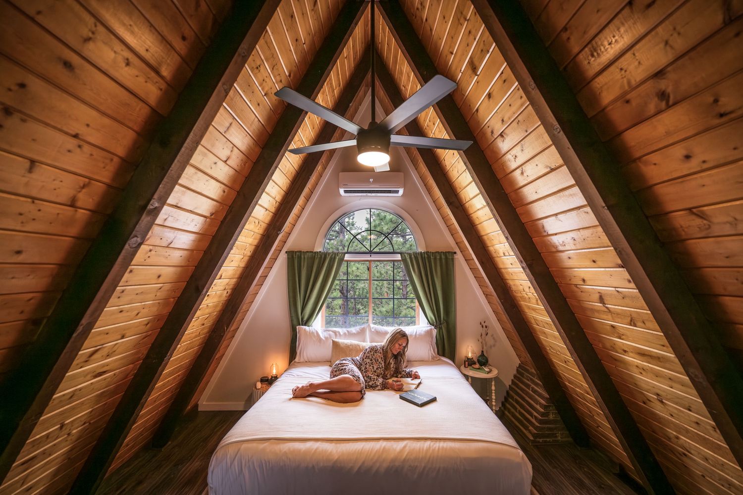 A woman reading a book on the bed in a short term rental property, Front Range A-frame in Bailey, CO.