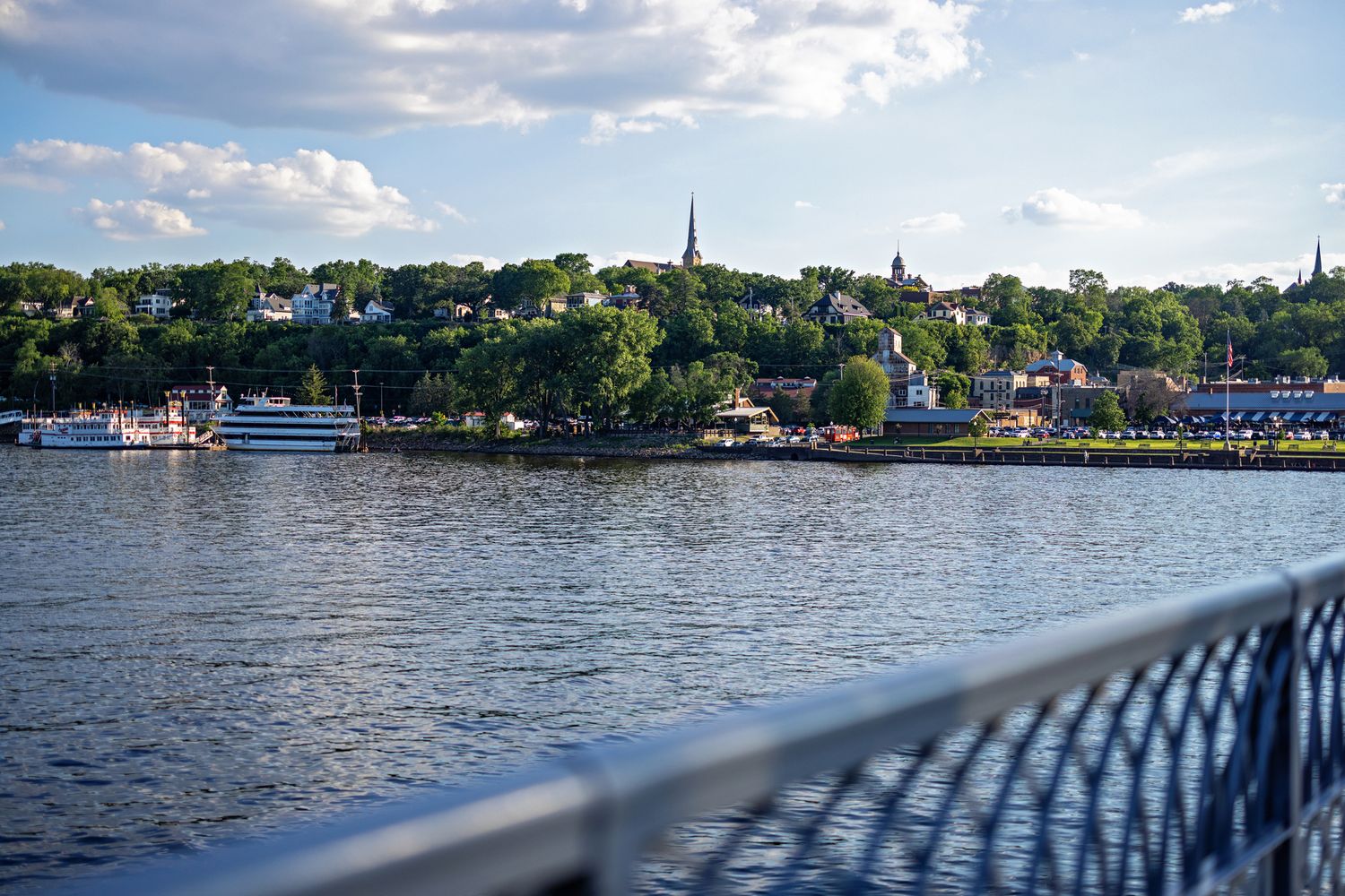 Scenic waterfront view of a charming town with church steeples and lush trees reflecting on calm blue water. Laura Leigh Imagaes.