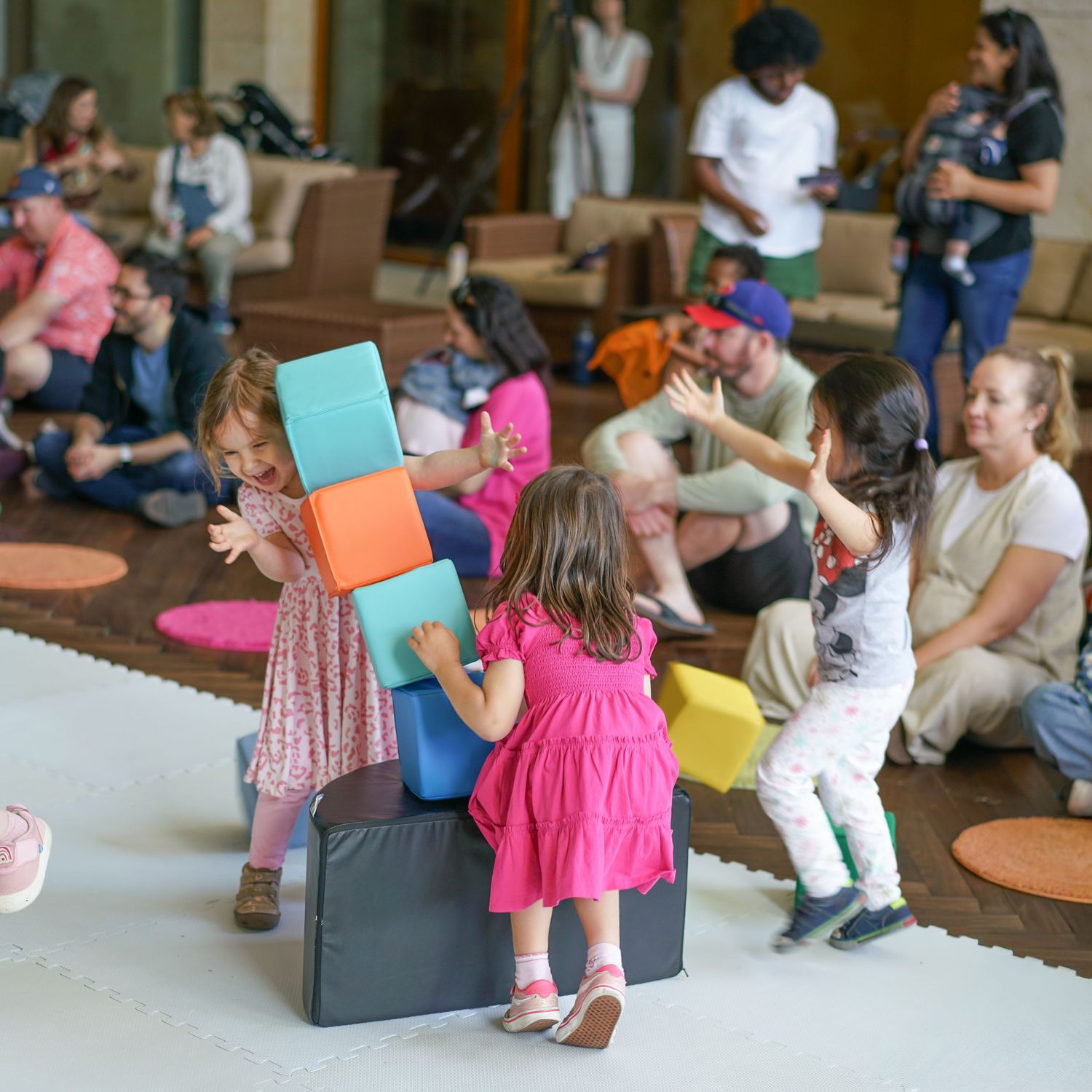 Children playing with colorful foam blocks while adults supervise in a bright indoor play area.
