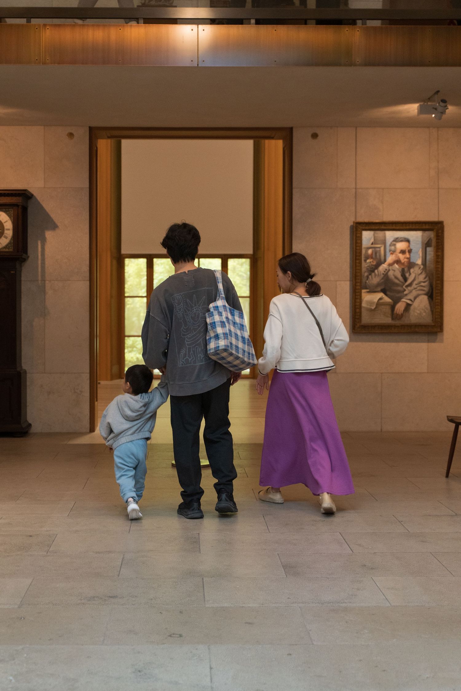 Family of three walking hand in hand through a museum gallery with artwork on display.