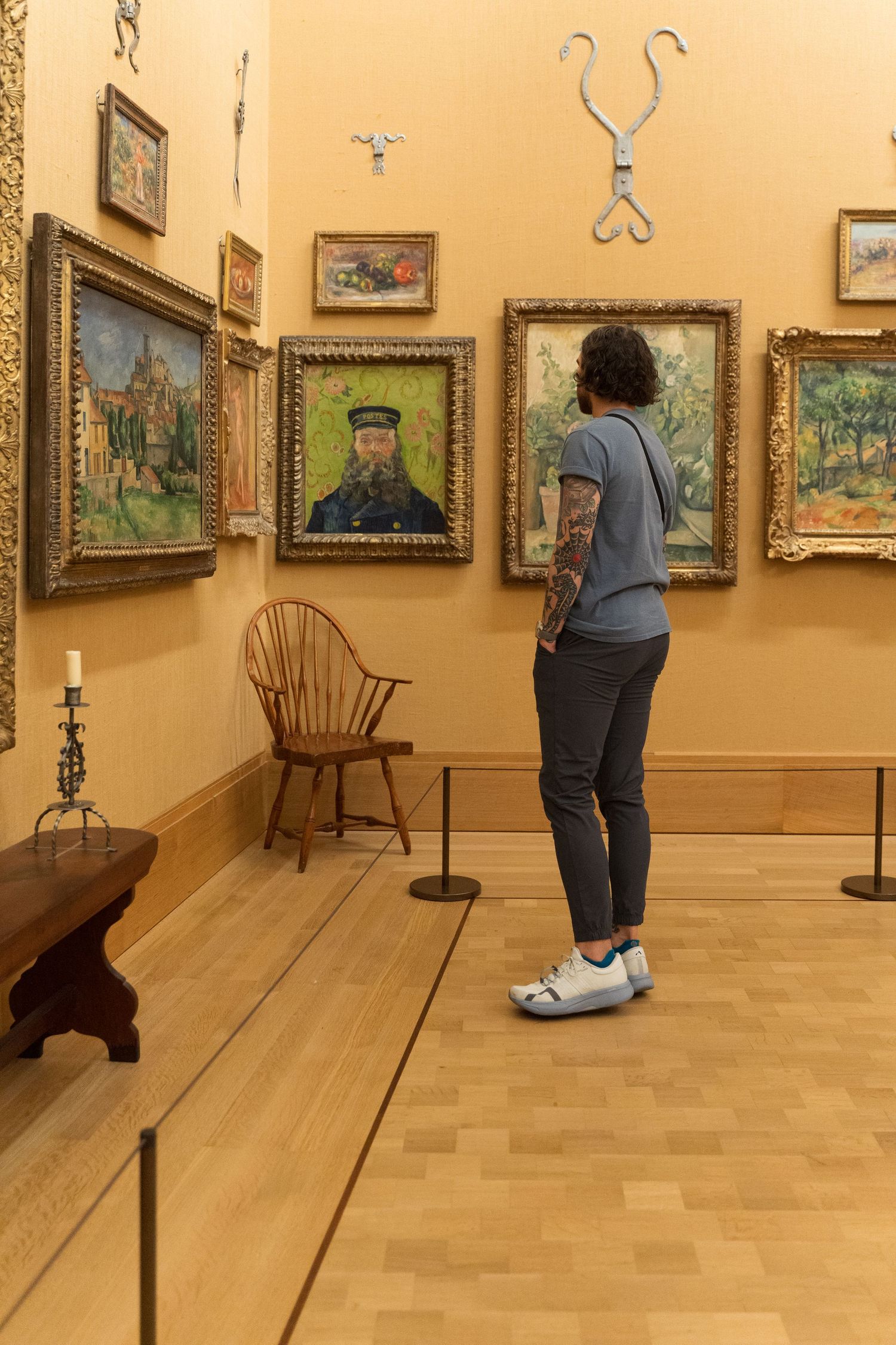 Tattooed visitor examines Van Gogh paintings on yellow walls in art museum gallery.