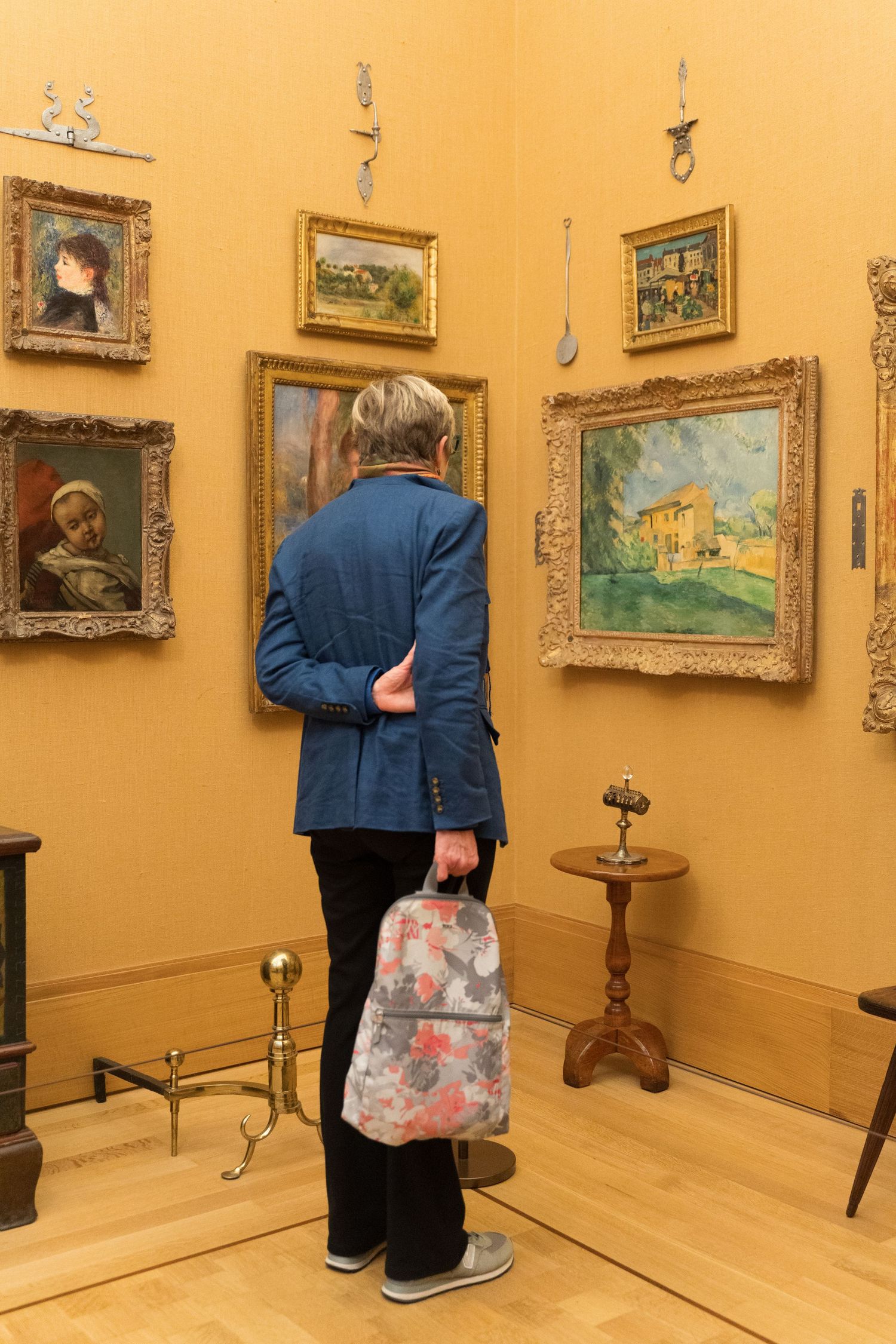 Senior visitor with backpack examining Impressionist paintings in museum gallery.