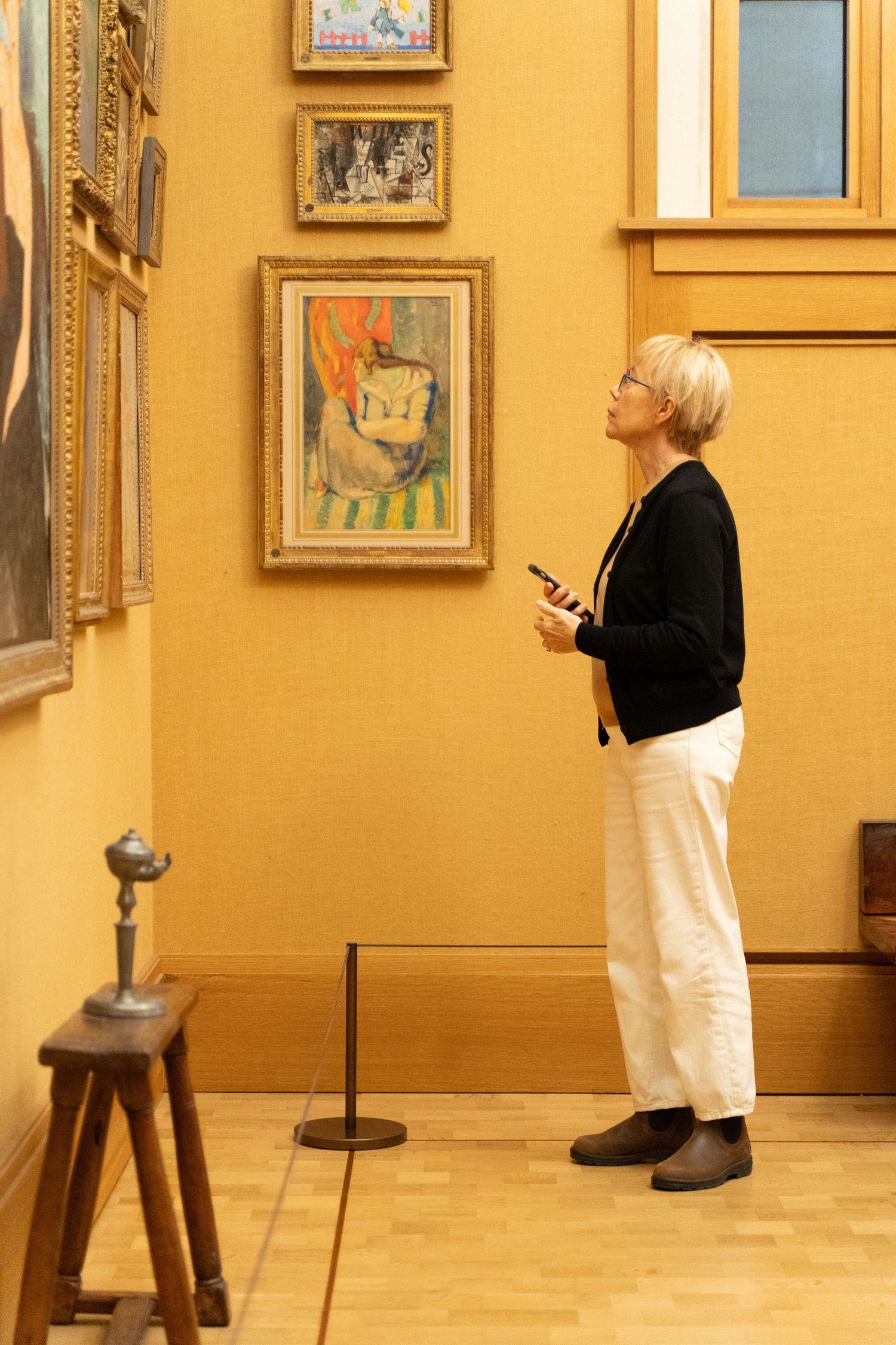 Blonde woman with phone admiring colorful artwork on golden museum gallery wall.