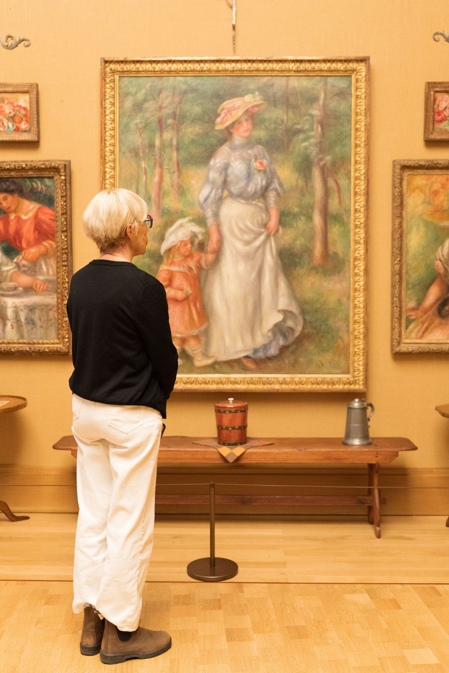 Senior woman viewing a large Renoir impressionist painting of a mother and child in an art gallery.