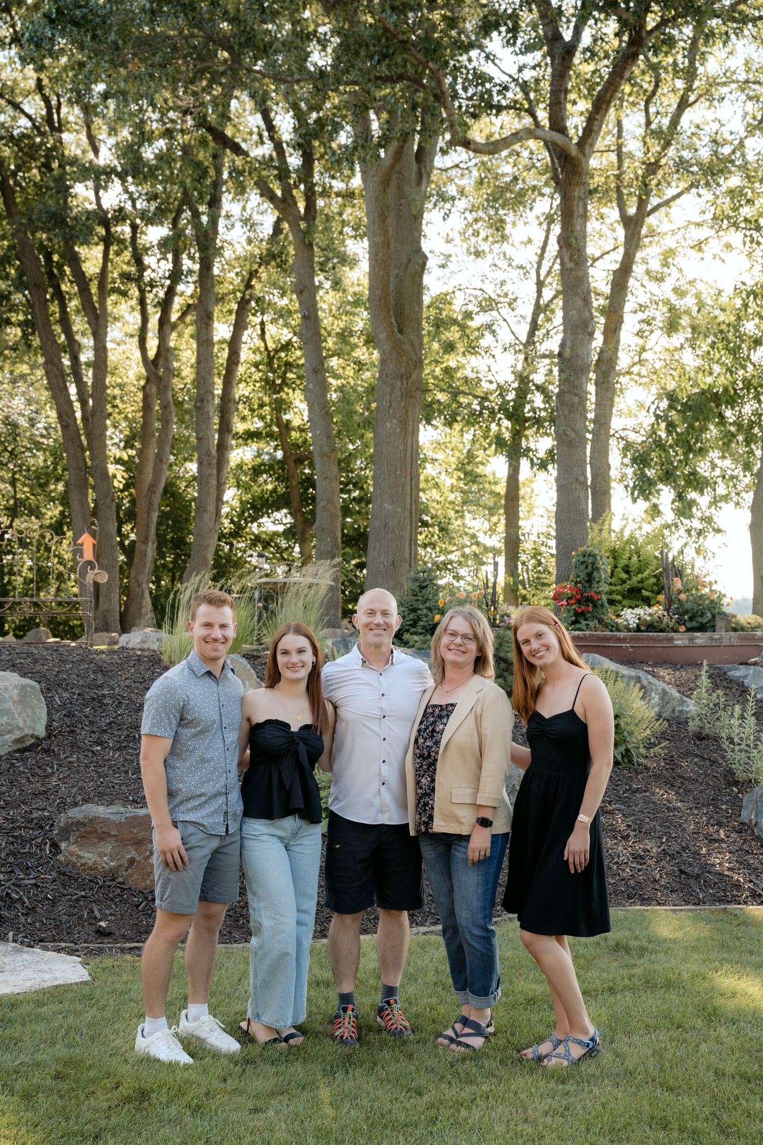 family of five stands in front of cabin gardens for summer family portraits on lake wissota in chippewa falls, wi