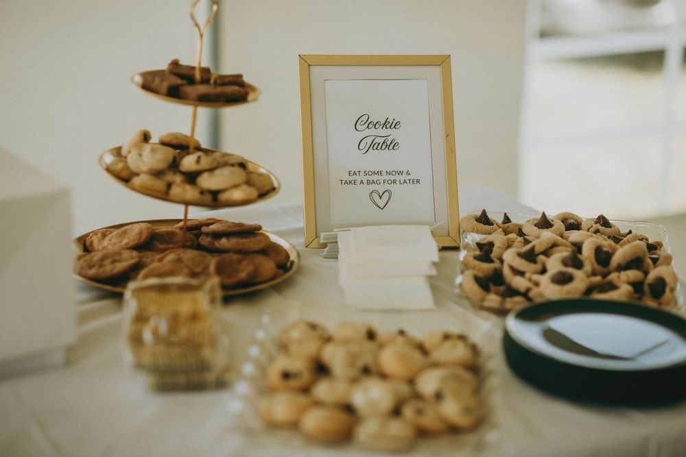 Elegant wedding cookie table display with tiered stand, assorted cookies, and a gold-framed sign reading Cookie Table.