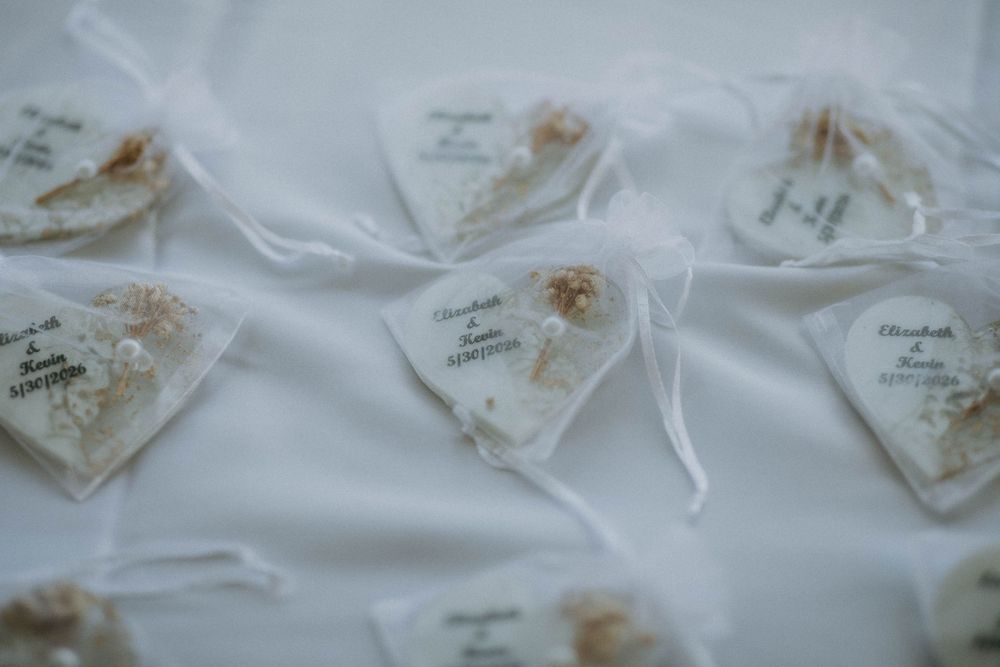 White organza wedding favor bags with personalized tags arranged on a white tablecloth.