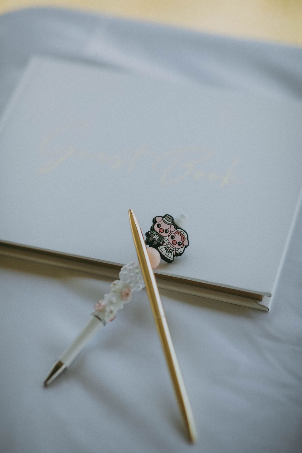 White wedding guest book with gold pen, floral pen, and sugar skull pin on soft white fabric.