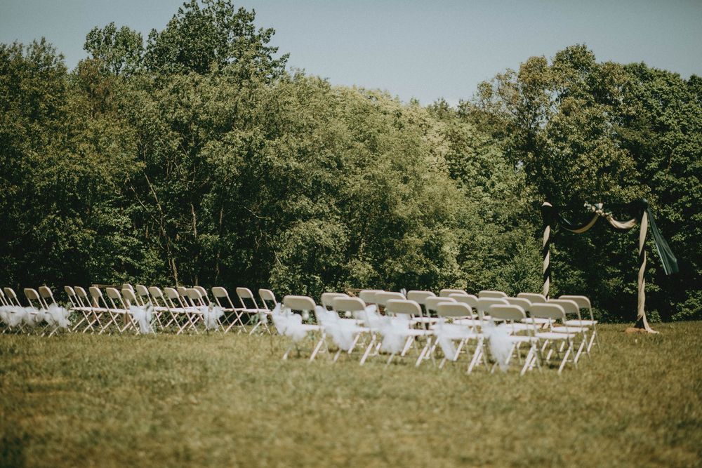 Rows of white folding chairs arranged on green grass for an outdoor wedding ceremony with lush trees in background.