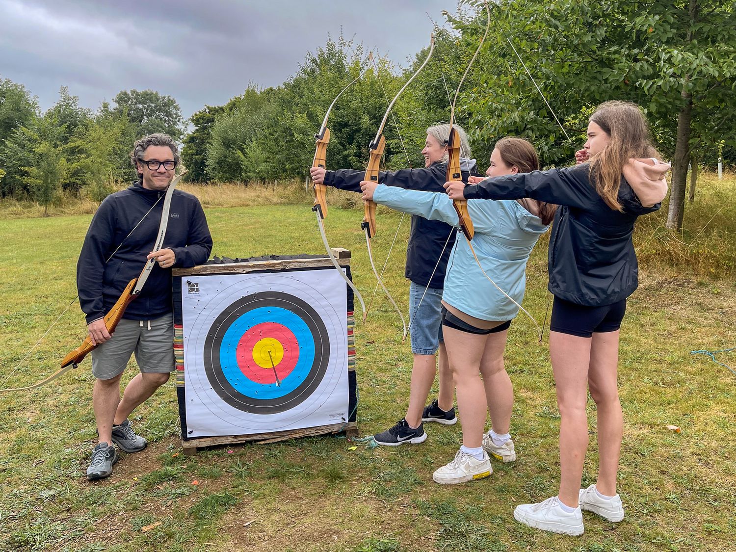 Group of people practicing archery outdoors, aiming bows at a colorful target on a green field.