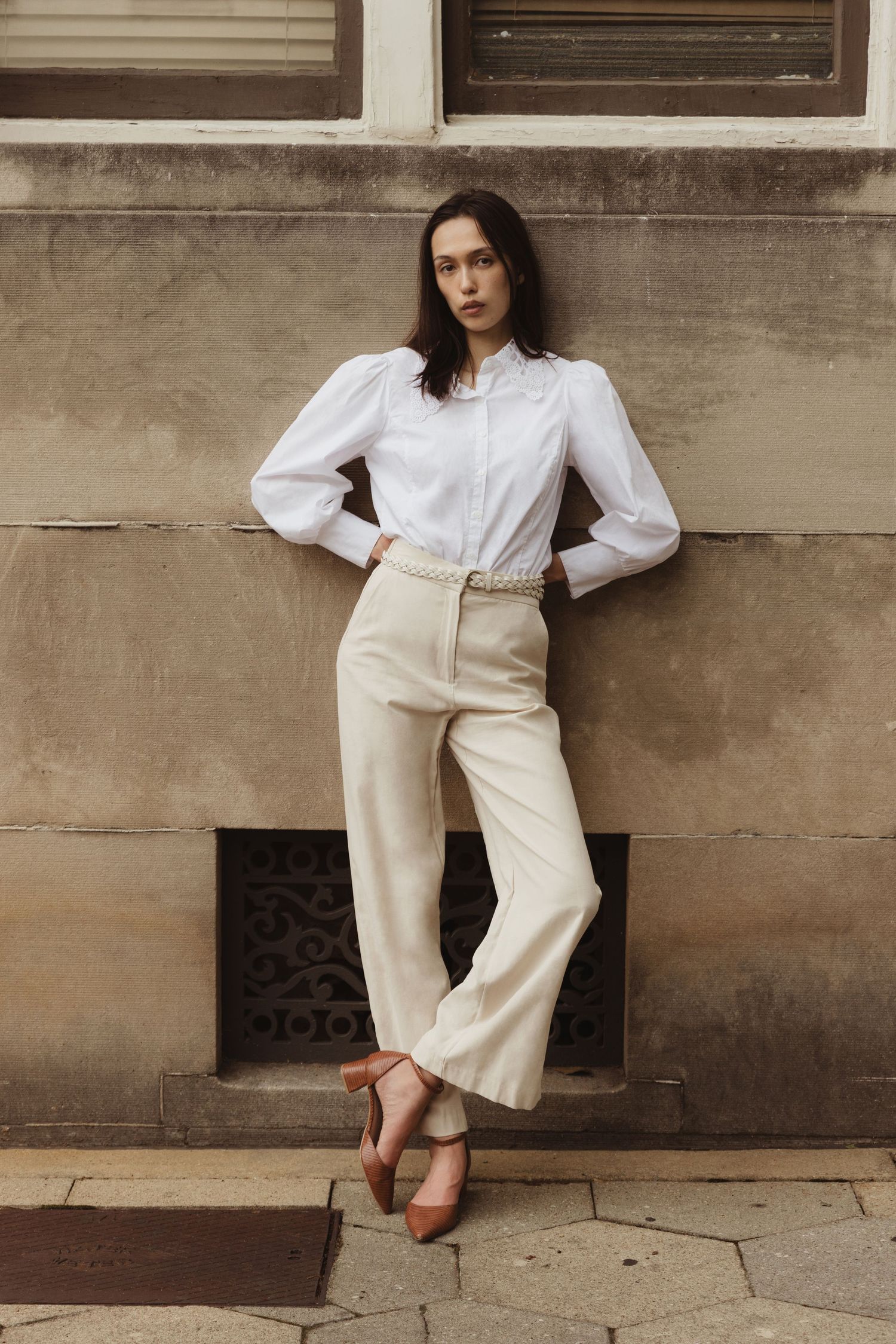 Editorial model leans on textured concrete wall in white blouse and cream trousers, Historic Downtown Atlanta fashion photography