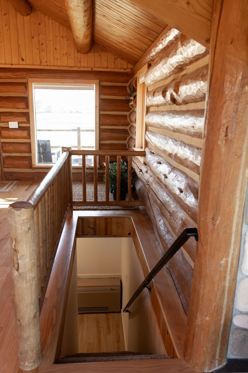 Interior view of a rustic log cabin staircase leading to a lower level, featuring natural wood walls and railings.