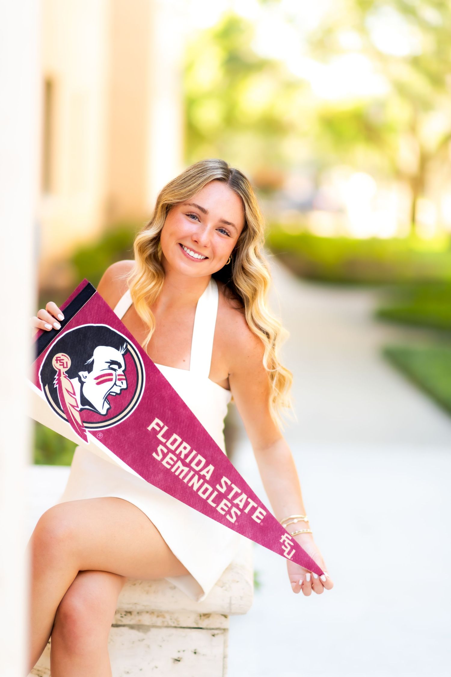 Smiling woman in white dress holding a Florida State Seminoles pennant flag.