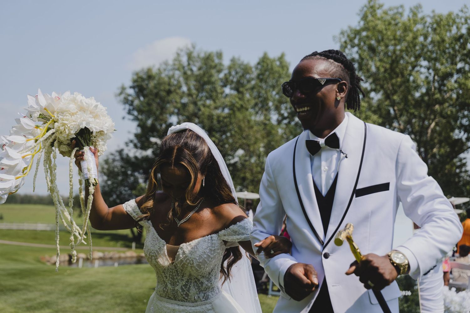 Bride and groom share a romantic moment under a white umbrella on a scenic overlook with forest and river views.
