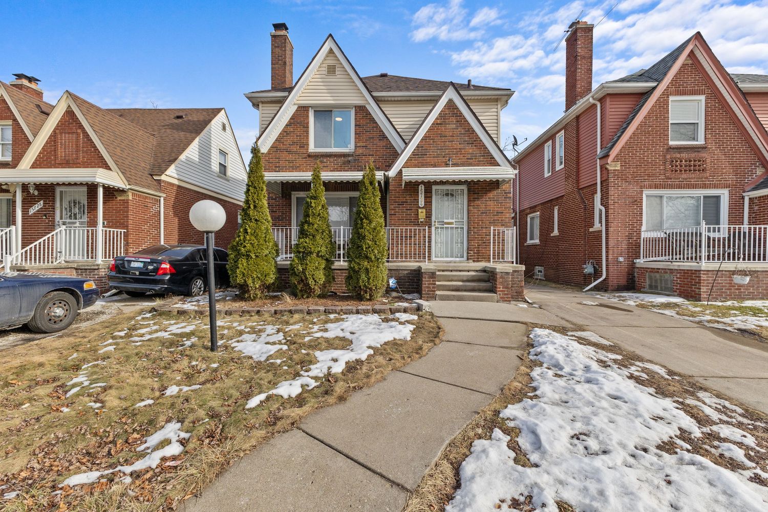Classic white clapboard bungalow with covered front porch, brick accent wall, and detached garage on a corner lot.