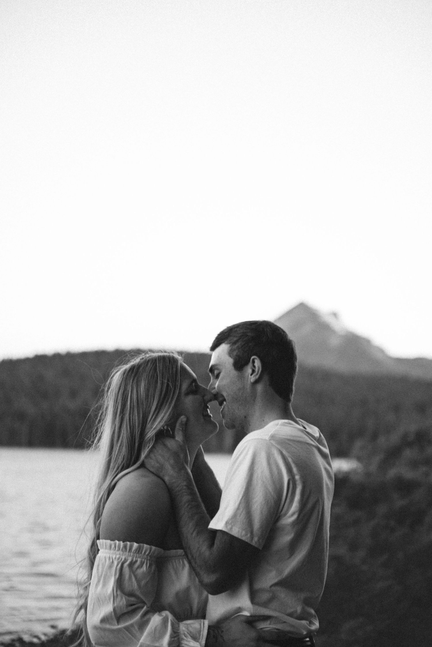 A couple in dark coats stands on a misty beach during an atmospheric photoshoot.