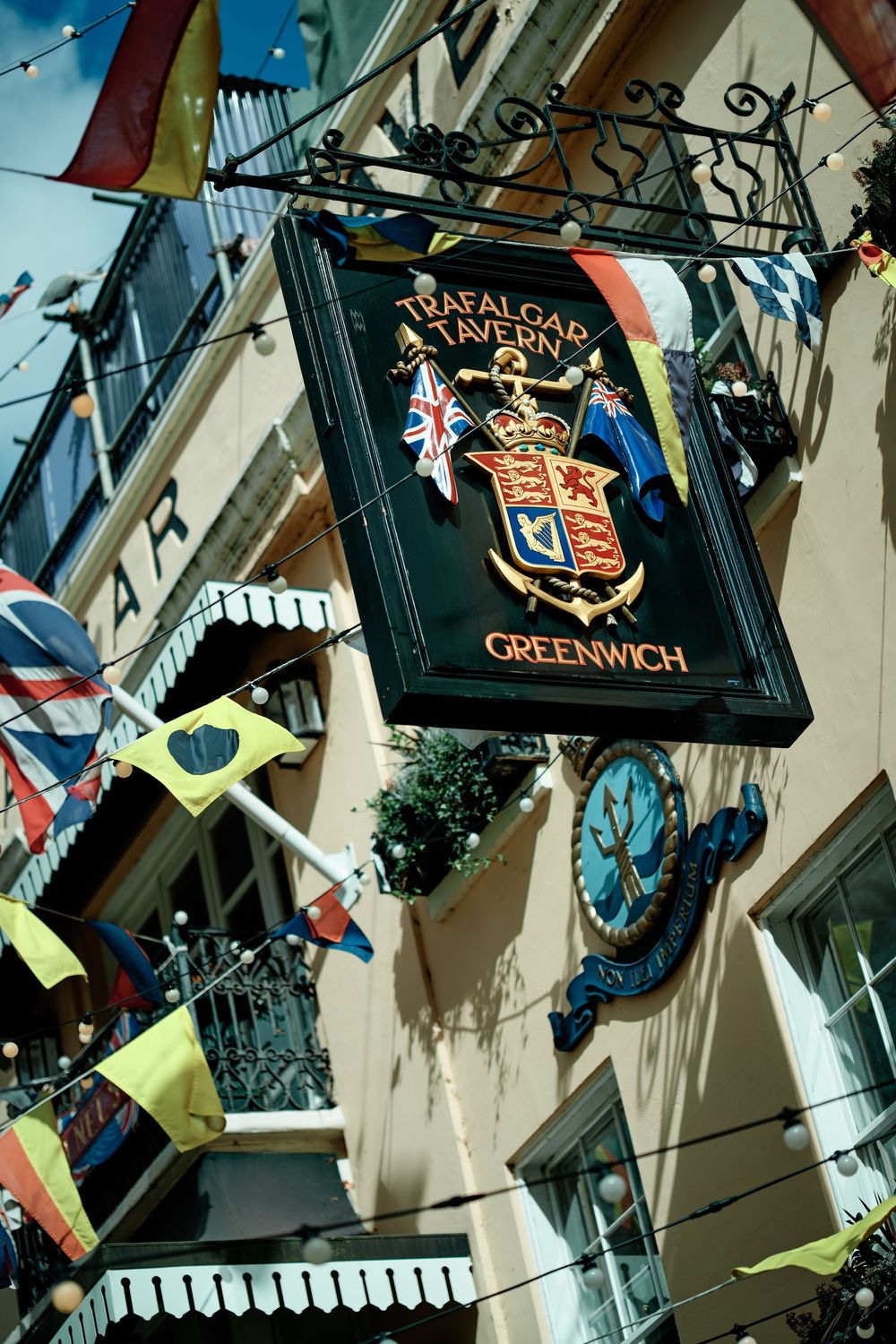 Trafalgar Tavern Greenwich pub sign with royal coat of arms, surrounded by colorful international flags on a historic building.