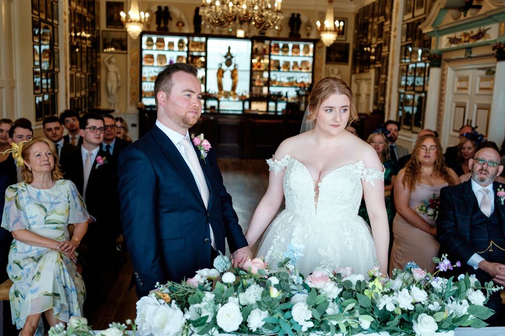 Bride and groom holding hands at wedding altar decorated with white roses and greenery in an elegant venue.