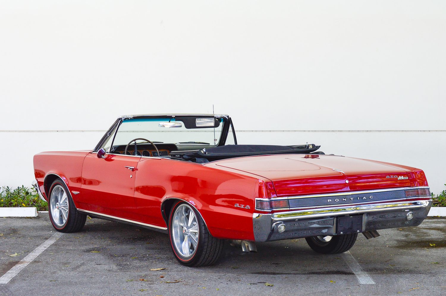 Red classic convertible muscle car parked, rear three-quarter view, chrome details, black soft top, custom wheels.