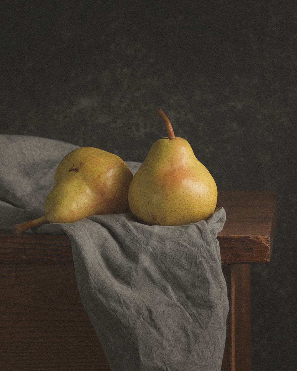 Two ripe yellow-green pears resting on a gray linen cloth draped over a wooden surface against a dark background.