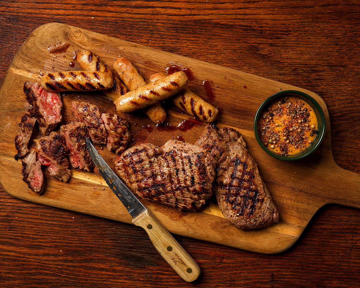 Assorted grilled meats on a wooden cutting board with a knife and dipping sauce, perfect for a steakhouse feast.