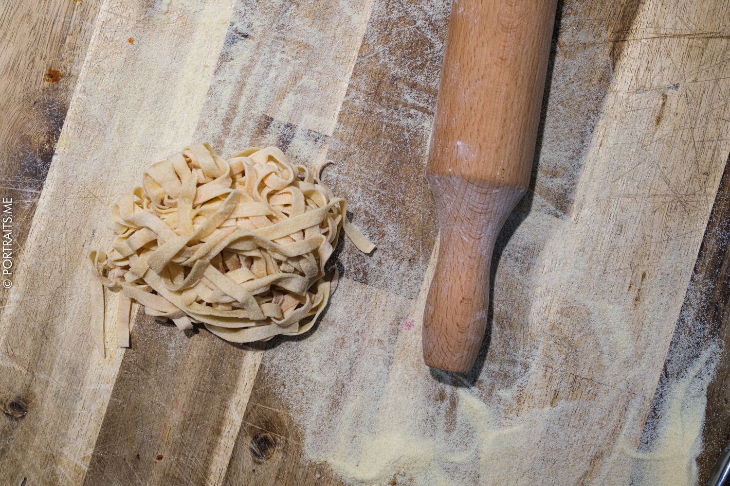 Fresh homemade pasta noodles on a floured wooden cutting board with a rolling pin.