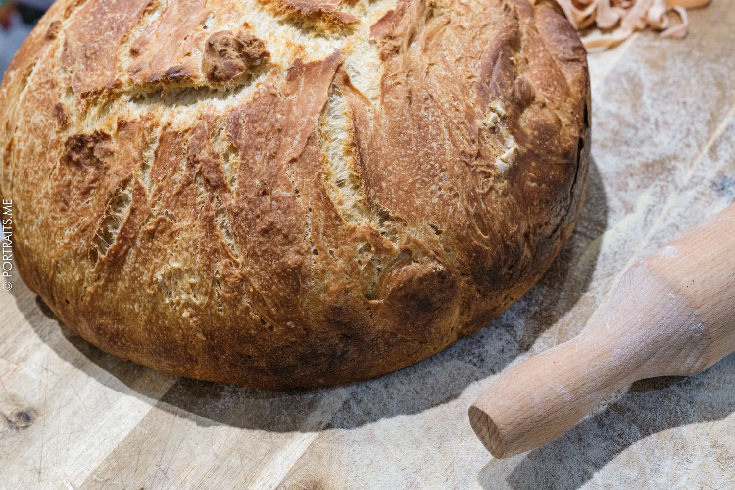Freshly baked rustic sourdough bread loaf with golden crust on parchment paper beside a wooden rolling pin.