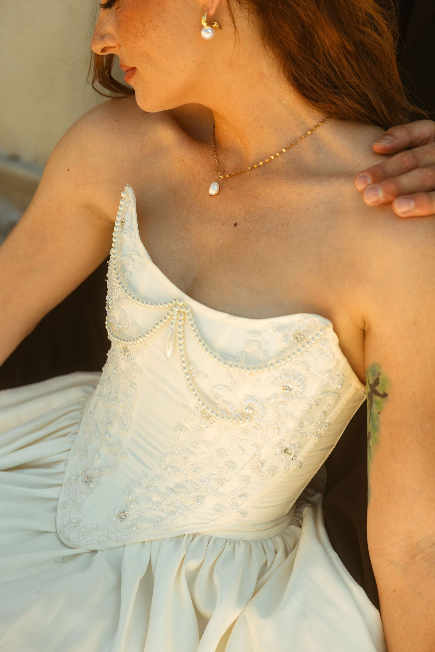Bride wearing a strapless white lace corset wedding gown with pearl details and delicate gold necklace.