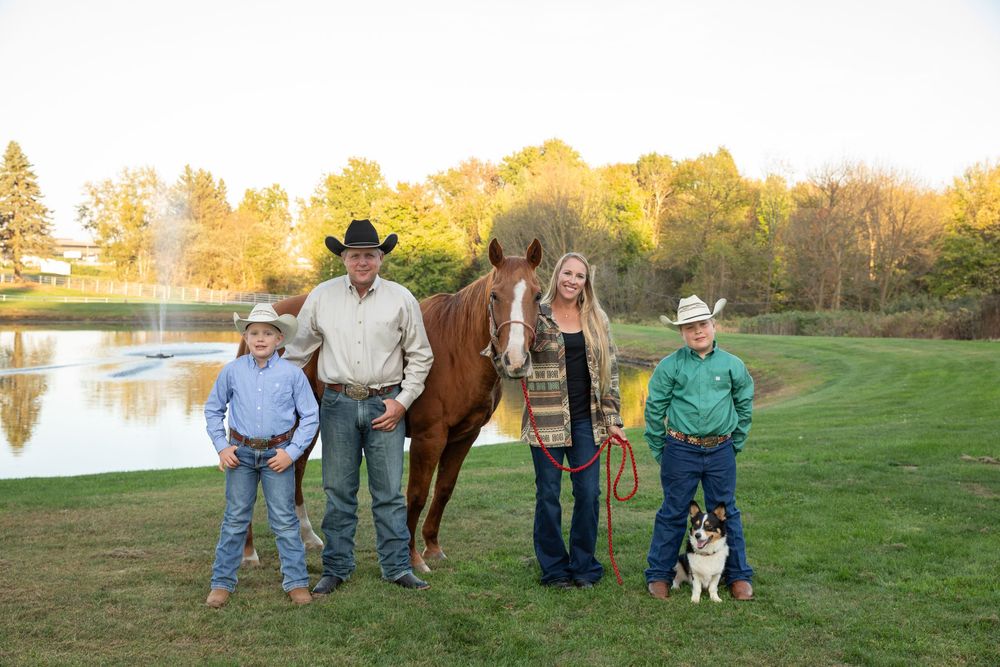 Family of four in western wear poses with a chestnut horse and dog by a scenic pond at golden hour.