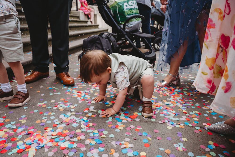 Baby crawling through colorful confetti on the ground after a wedding ceremony.