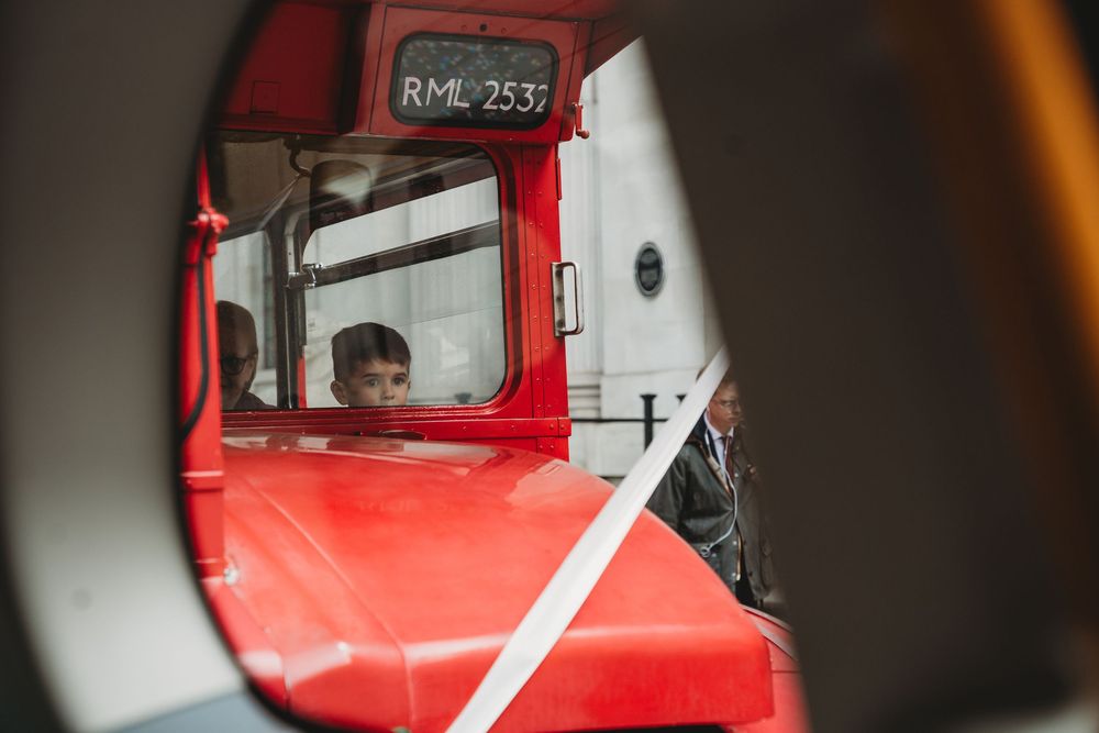 Young boy peering through circular window of a vintage red double-decker bus RML2537.