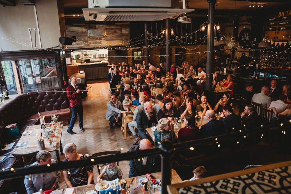 Aerial view of a packed wedding reception in a rustic venue with fairy lights and long dining tables.
