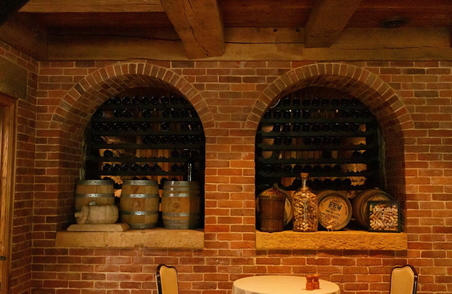 Rustic brick wine cellar with arched niches displaying wooden barrels and decorative copper vessels on stone shelves.
