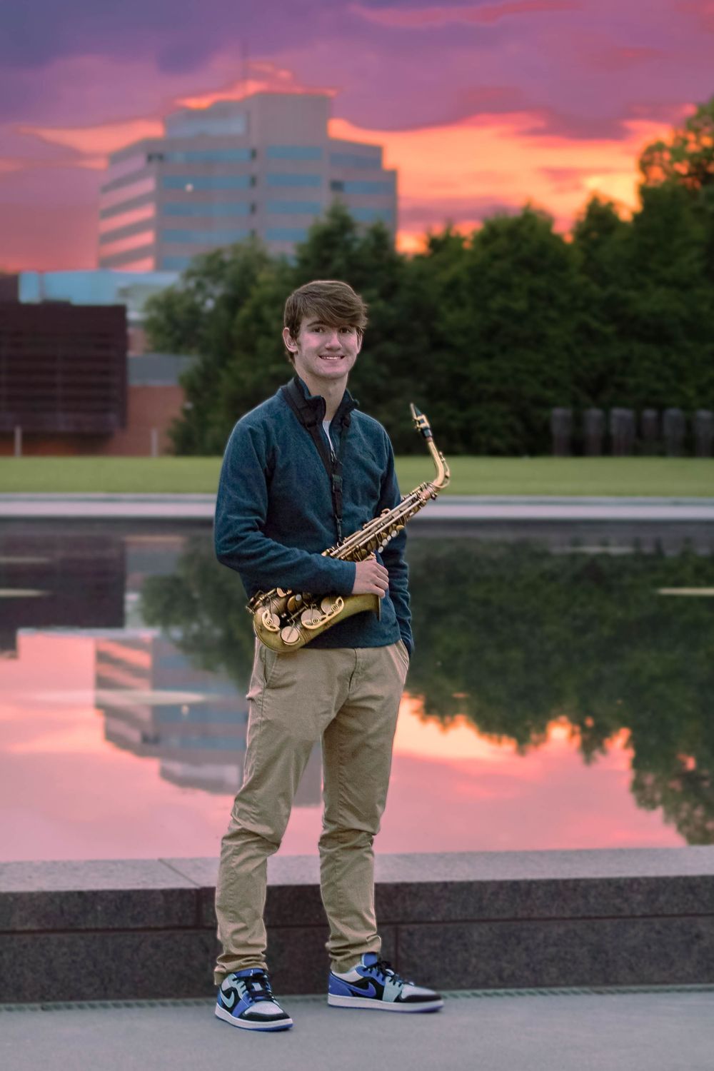 Senior photo in Kansas City at sunset with his saxophone and the city in the background.