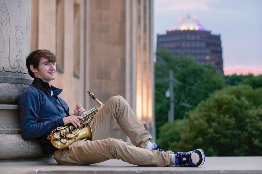 Senior photo in Kansas City at sunset with his saxophone and the city in the background.