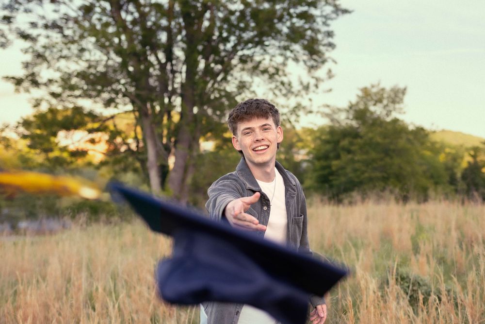 Senior photo in Charlottesville, VA at golden hour with hat being thrown to the camera.