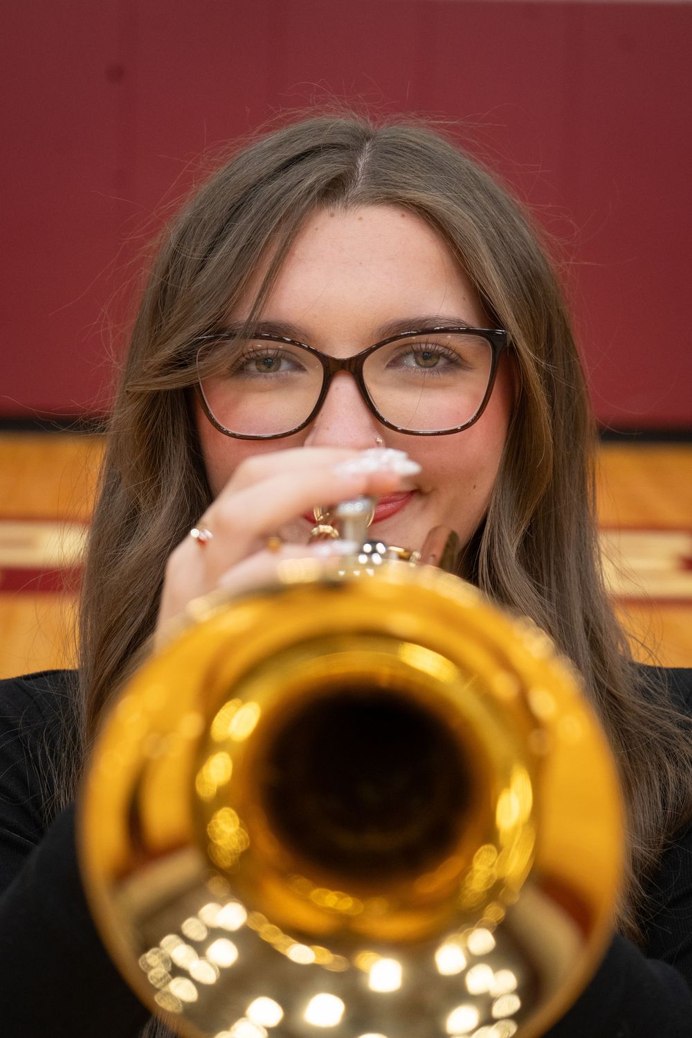 Young woman with glasses playing a shiny gold trumpet, close-up portrait shot in a concert hall.