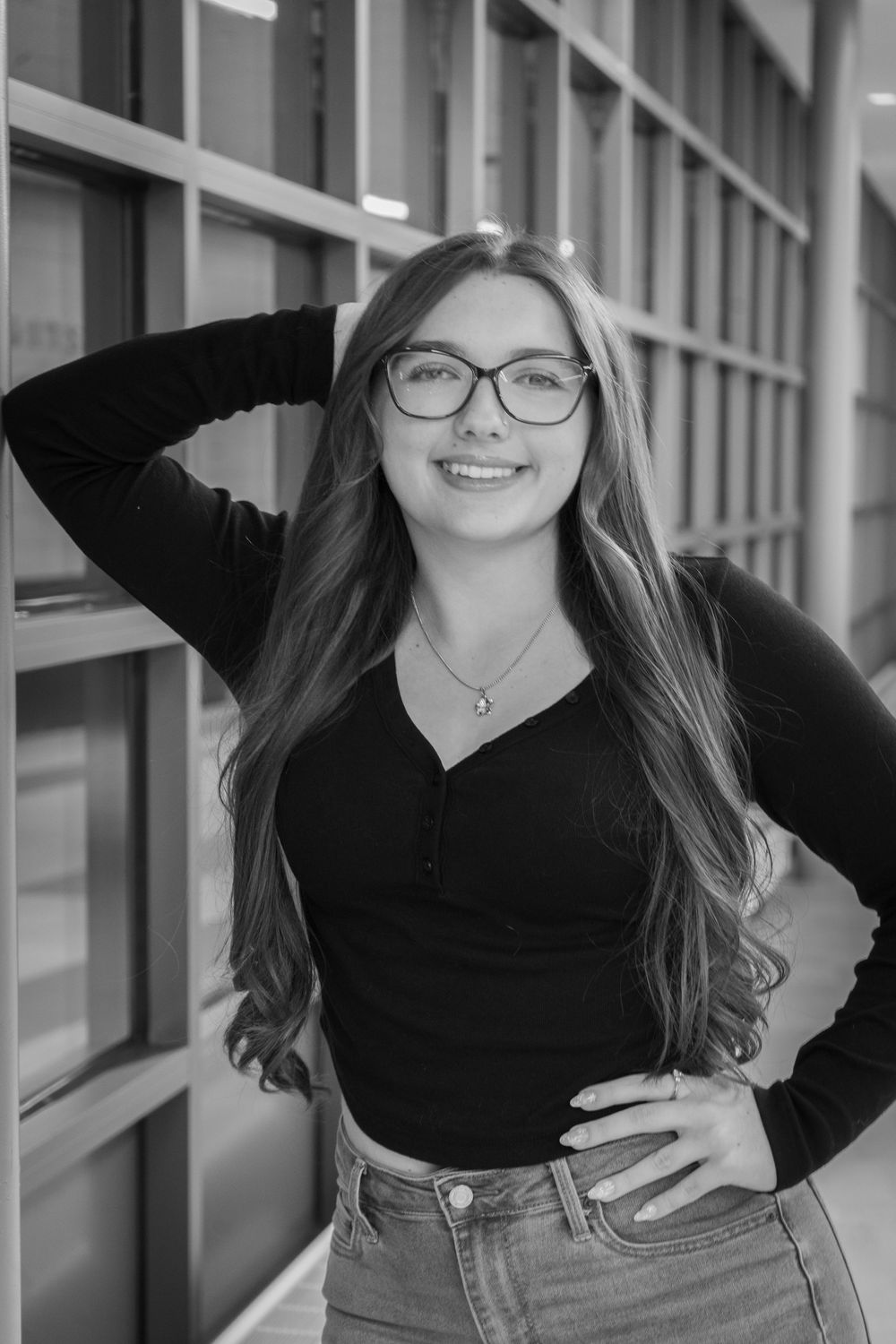 Young woman with glasses and long hair smiling confidently, posing in black and white portrait photo.
