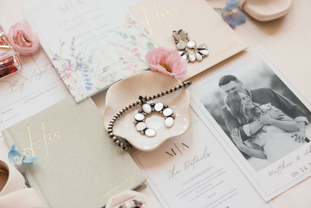 Wedding flat lay with floral invitations, jewelry, and black-and-white couple photo on neutral background. Bell Manor Chillicothe Ohio.