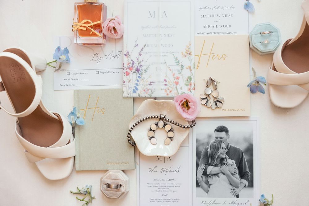 Wedding flat lay featuring floral invitations, gold rings, blush heels, and elegant accessories.