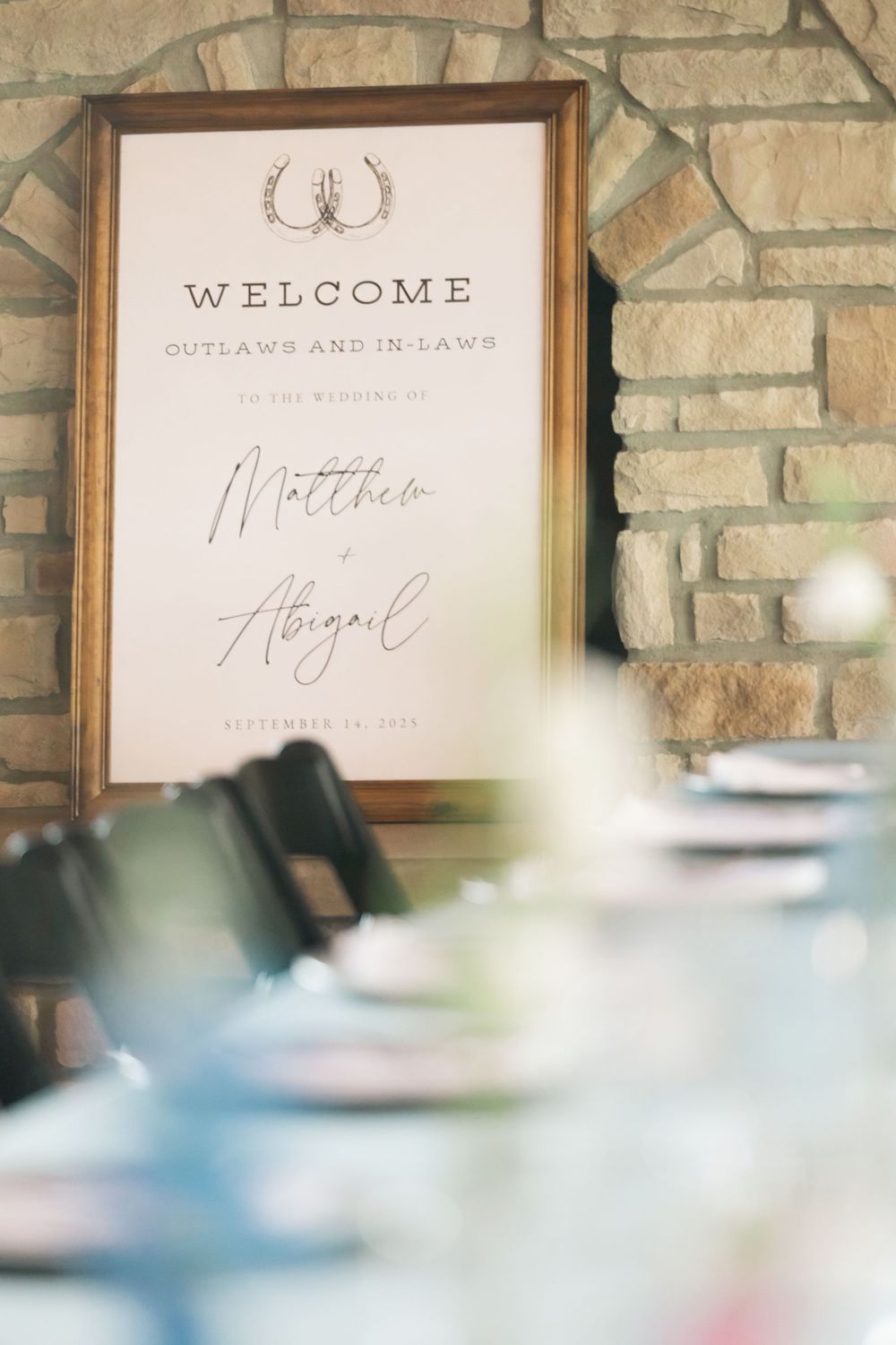 Rustic wedding welcome sign reading Outlaws and In-Laws for Matthew and Abigail on stone wall.