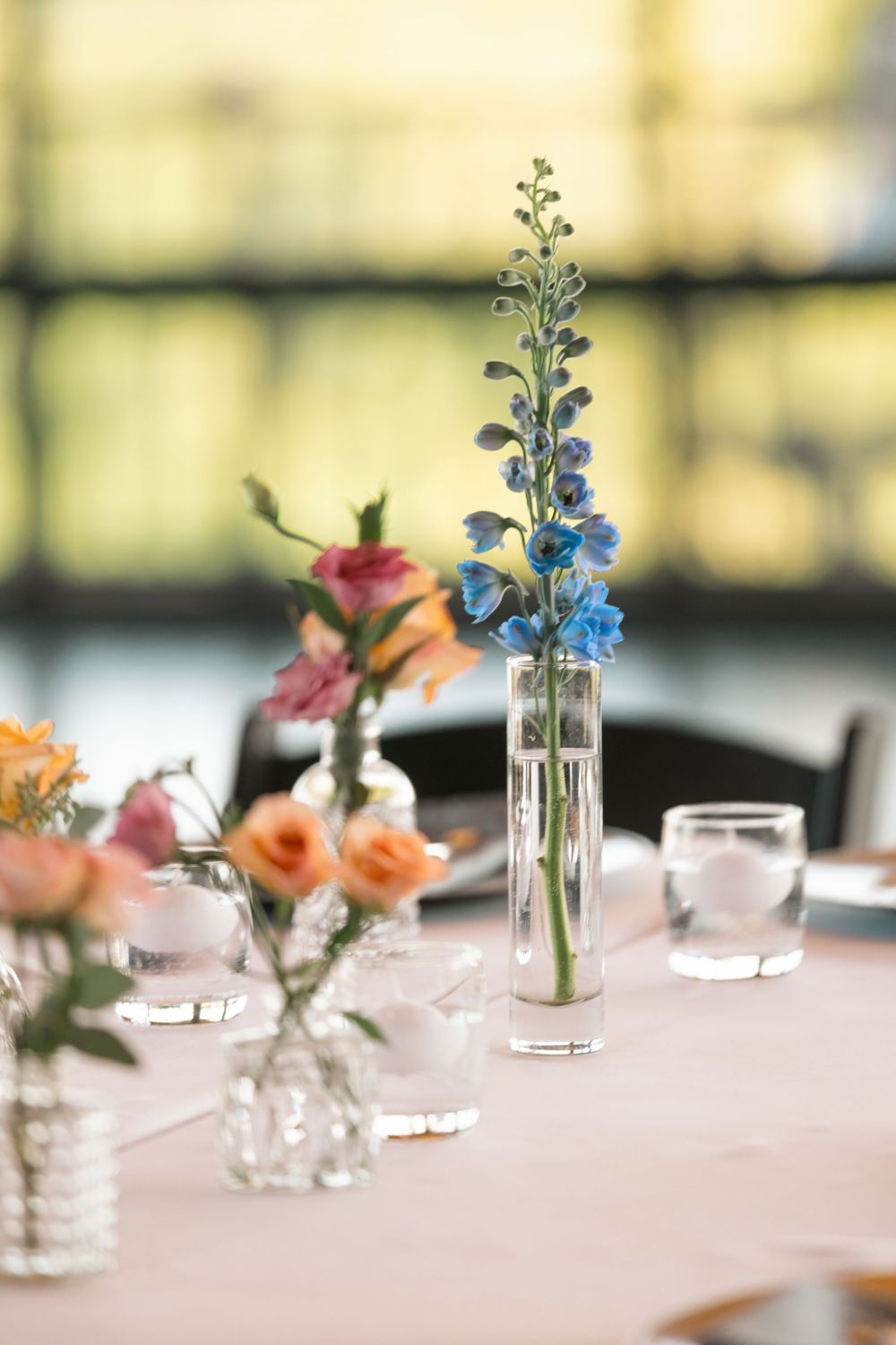 Elegant wedding table centerpiece with blue delphinium and peach roses in glass bud vases.