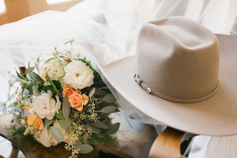 Tan felt cowboy hat resting beside a bridal bouquet of white and peach flowers.