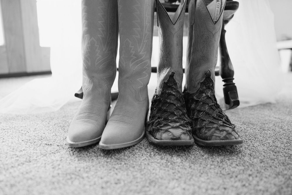 Black and white photo of bride and groom cowboy boots side by side on carpet.